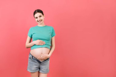 Çıplak hamile kadının göbeği renkli arka planda açık kot pantolon ve fotokopi alanı. Hamilelik konsepti.