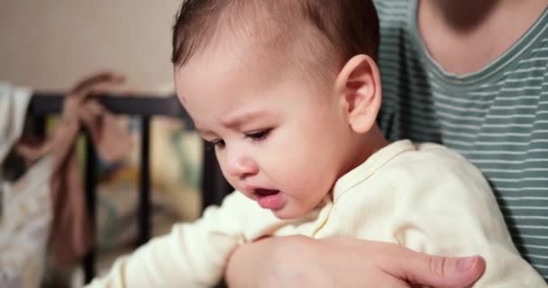 Eine junge Mutter hält einen schönen sieben Monate alten Sohn, der lächelt und an Fingern und Mutterhand nagt. Juckende Zähne eines Neugeborenen, Kinderkrankheiten. Zeitlupe — Stockvideo