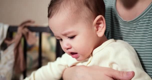 Una giovane madre sta tenendo in braccio un bellissimo figlio di sette mesi che sorride e rode le dita e la mano della madre. denti pruriginosi di un neonato, dentizione. rallentatore — Video Stock