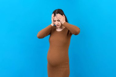 Güzel, genç, hamile bir kadın, renkli bir arka planda baş ağrısı çekiyor. Stresli hamile kadın ya da anne sorunları.