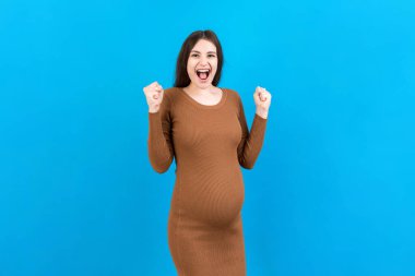 Renkli arka planda genç, güzel, hamile bir kadın kollarını kaldırıp, gözleri açık bir şekilde başarıyı kutluyor. Kazanan konsept.