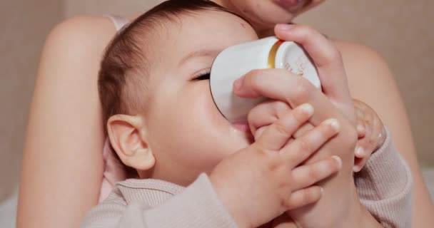 Retrato de un niño pequeño que se sienta en brazos de su madre. El niño feliz bebe leche o productos lácteos de una taza. Nutrición adecuada y natural para los niños — Vídeo de stock
