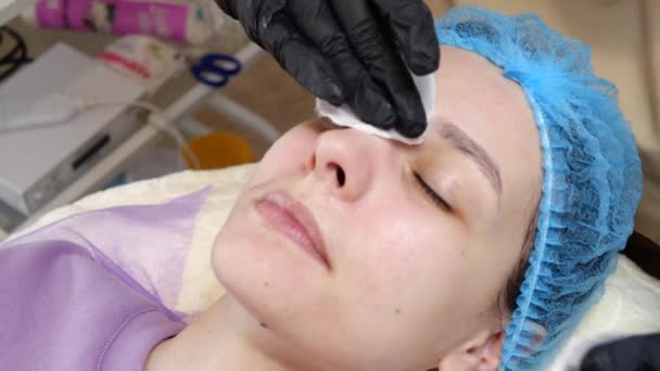 Close-up, cosmetician em luvas médicas aplica uniformemente creme cosmético ou protetor solar para o rosto feminino após o descascamento. conceito de cuidados com a pele e proteção solar. cosmetologia em salão de beleza — Vídeo de Stock