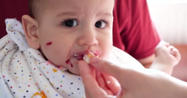 Mother holds the baby in her arms and feeds her boy with a spoon. family, food, child, eating and parenthood concept — Stock Video