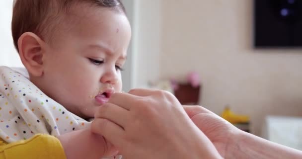 Mamma håller barnet i sina armar och matar sin pojke med en sked. familj, mat, barn, mat och föräldraskap — Stockvideo