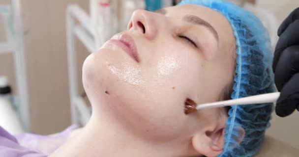 Cosmetólogo está aplicando mascarilla peeling en la cara de las mujeres usando cepillo en clínica de belleza. Esteticista haciendo el procedimiento de cuidado de la piel. Tratamiento de spa en cosmetología — Vídeo de stock