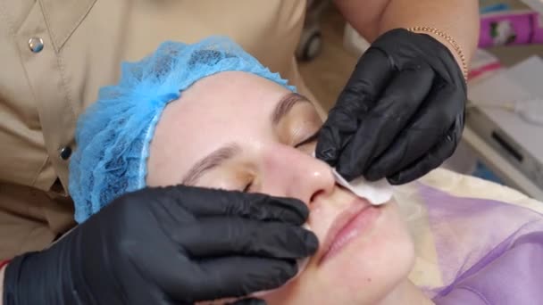 Close-up, cosmetician in medical gloves applies evenly cosmetic cream or sunscreen to female face after peeling. skincare and sun protection concept. cosmetology on beauty salon — Stock Video