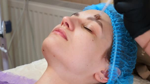 Cosmetologist εφαρμόζει peeling μάσκα σε γυναίκες πρόσωπο χρησιμοποιώντας βούρτσα στην κλινική ομορφιάς. Όμορφος κάνει τη διαδικασία φροντίδας του δέρματος. Spa θεραπεία στην κοσμετολογία — Αρχείο Βίντεο