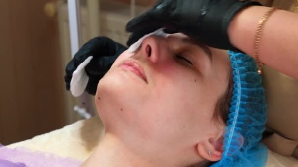 Cosmetologist doctor wiping woman face uses cotton pads after peeling procedure. Doctor is making beauty procedure in cosmetology clinic. Care about face skin — Stock Video