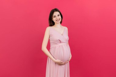 Mutlu hamile kadın renkli arka planda karnına dokunuyor. Müstakbel anne beyaz iç çamaşırı giyiyor. Bir bebek bekliyorduk. Boşluğu kopyala.