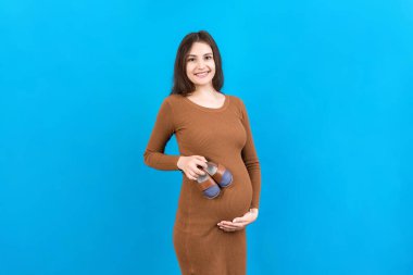 Renkli arka planda bir erkek bebeğe küçük çizmeler gösteren mutlu hamile kadın. Müstakbel anne bir çocuk bekliyor. Boşluğu kopyala.