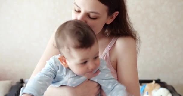 Mãe segura o bebê em seus braços e brinca com ele. Pouco bonito filho brinca com a mãe em casa — Vídeo de Stock