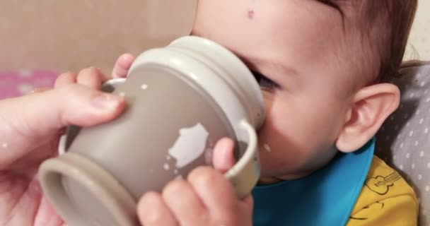 귀여운 사내 아이 가 집에서 물 한 컵을 마시고 있군. 클로즈업. 아이는 플라스틱 빨대 컵에서 물을 마신다 — 비디오