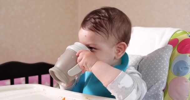 귀여운 사내 아이 가 집에서 물 한 컵을 마시고 있군. 클로즈업. 아이는 플라스틱 빨대 컵에서 물을 마신다 — 비디오