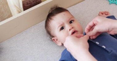 Annem küçük bir çocuğu yatakta giydirir. Tıp, sağlık, aile, masumiyet, pediatri, mutluluk bebek kavramları