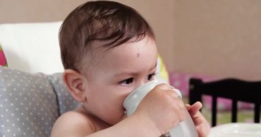 Evde bir bardak su içen tatlı bir erkek bebek. Yakın plan. Çocuk plastik bir biberondan su içiyor.