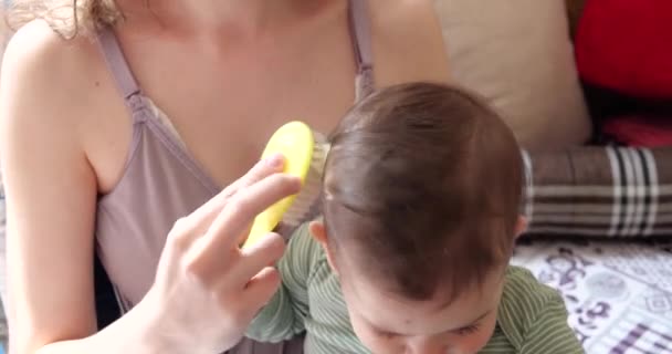 Mãe penteando o cabelo na cabeça do bebê enquanto ele se senta nos braços da mãe — Vídeo de Stock