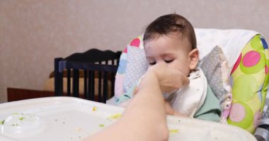Anne çocuğu kaşıkla ve elle besler, aile yemeği ve ebeveynlik konseptiyle. İlk tamamlayıcı gıda ve kendini besleme.