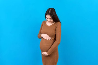 Mutlu hamile kadın renkli arka planda karnına dokunuyor. Müstakbel anne beyaz iç çamaşırı giyiyor. Bir bebek bekliyorduk. Boşluğu kopyala.
