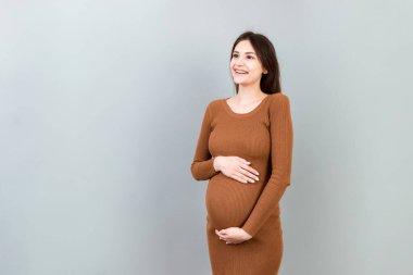 Mutlu hamile kadın renkli arka planda karnına dokunuyor. Müstakbel anne beyaz iç çamaşırı giyiyor. Bir bebek bekliyorduk. Boşluğu kopyala.