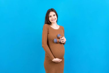 Renkli arka planda bir erkek bebeğe küçük çizmeler gösteren mutlu hamile kadın. Müstakbel anne bir çocuk bekliyor. Boşluğu kopyala.