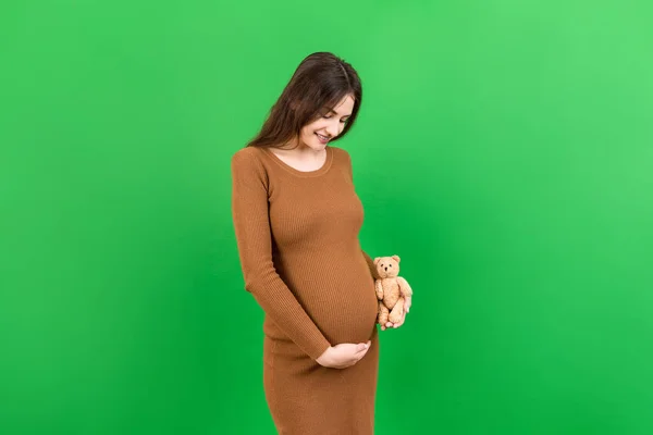 在彩色背景下 快乐的孕妇抱着一只泰迪熊靠着她的腹部 年轻的母亲怀孕了 复制空间 — 图库照片
