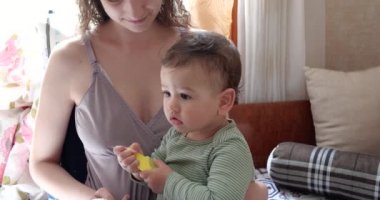 Anne, anne kollarında otururken bebeğin saçlarını tarıyor.