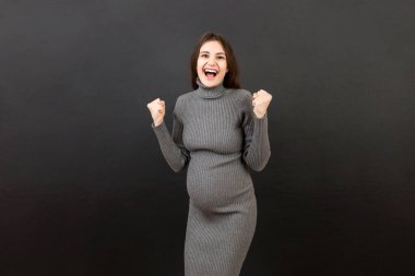 Renkli arka planda genç, güzel, hamile bir kadın kollarını kaldırıp, gözleri açık bir şekilde başarıyı kutluyor. Kazanan konsept.