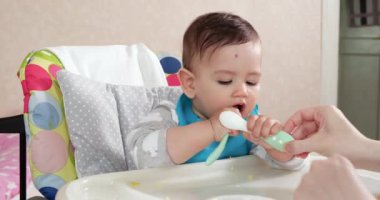 Anne çocuğu kaşıkla ve elle besler, aile yemeği ve ebeveynlik konseptiyle. İlk tamamlayıcı gıda ve kendini besleme.