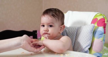 Anne çocuğu kaşıkla ve elle besler, aile yemeği ve ebeveynlik konseptiyle. İlk tamamlayıcı gıda ve kendini besleme.