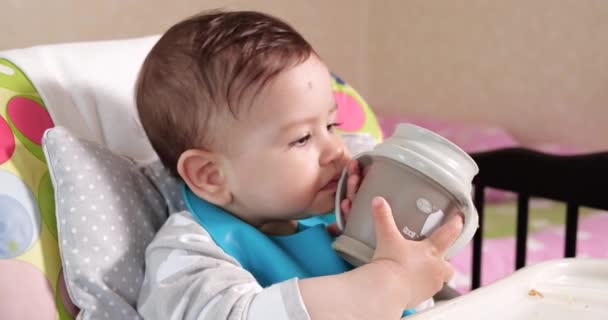 Lindo niño bebiendo un vaso de agua en casa. Primer plano. El niño bebe agua de una taza de plástico — Vídeos de Stock