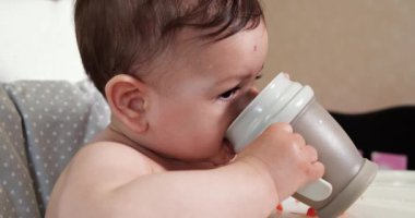 Evde bir bardak su içen tatlı bir erkek bebek. Yakın plan. Çocuk plastik bir biberondan su içiyor.