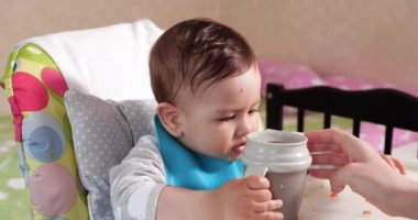 Anne çocuğu kaşıkla ve elle besler, aile yemeği ve ebeveynlik konseptiyle. İlk tamamlayıcı gıda ve kendini besleme.