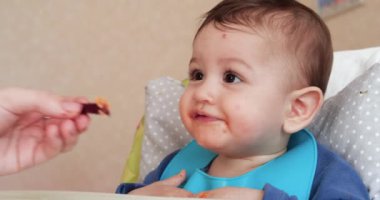 Anne çocuğu kaşıkla ve elle besler, aile yemeği ve ebeveynlik konseptiyle. İlk tamamlayıcı gıda ve kendini besleme.