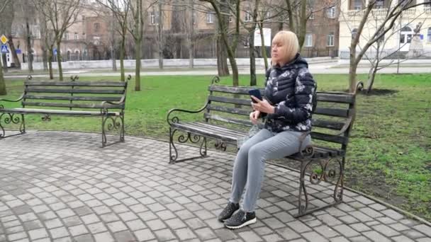 A woman sits on a bench in the park and opens an umbrella — Vídeo de stock
