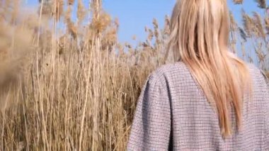 Bir kadın, nehir kenarındaki sazlıklar boyunca düşünceli bir şekilde yürür, açık bir günde, mavi gökyüzünde.