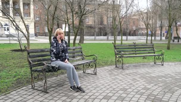 A woman sits on a bench in the park and opens an umbrella — Vídeo de stock