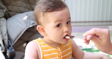 Anne bebeği kollarında tutuyor ve oğlunu kaşıkla besliyor. aile, yemek, çocuk, yeme ve ebeveynlik kavramı