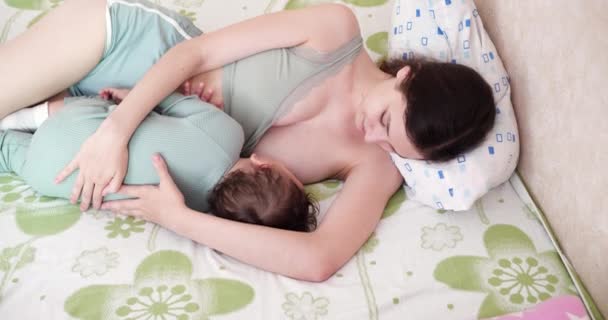 Happy mom smiles with happiness breastfeeds her little son in the bed — Stock Video