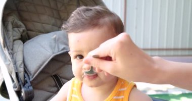 Anne bebeği kollarında tutuyor ve oğlunu kaşıkla besliyor. aile, yemek, çocuk, yeme ve ebeveynlik kavramı