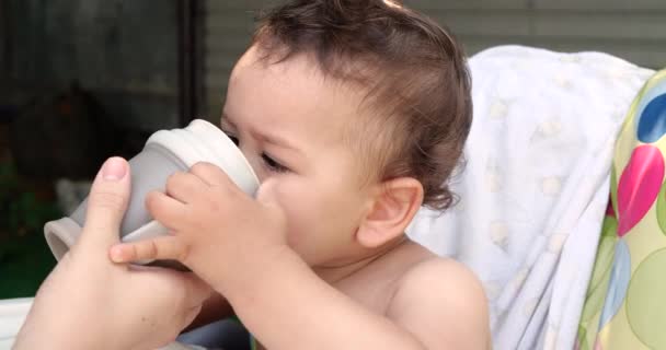 Rapaz giro a beber um copo de água num café. A criança bebe água de um copo fora depois de comer — Vídeo de Stock