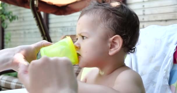 Retrato de un niño que se sienta en una silla infantil. El niño feliz bebe leche, kéfir o productos lácteos de una taza. Nutrición correcta y natural para niños — Vídeos de Stock