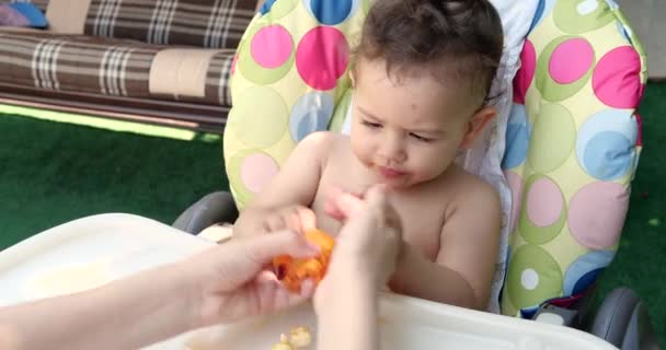 Een klein kind zit op een babystoel en eet in de zomer een perzik. Het concept van de jeugd. Close-up opname — Stockvideo