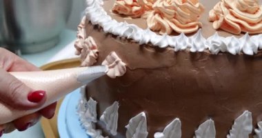 Elinde pasta poşeti olan bir kadın pasta şefi ev mutfağında pastaya krema sıkıyor. Fırın mutfağında çalışan profesyonel bir şef. Yemek pişirme, yemek pişirme, ev yemeği.