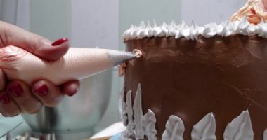 Elinde pasta poşeti olan bir kadın pasta şefi ev mutfağında pastaya krema sıkıyor. Fırın mutfağında çalışan profesyonel bir şef. Yemek pişirme, yemek pişirme, ev yemeği.