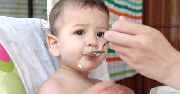 Portret van een kind dat babyvoeding eet met zijn lepel. moeder voedt het kind buiten aan de kindertafel — Stockvideo