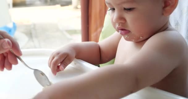 Portrait d'un enfant qui mange de la nourriture pour bébé avec sa cuillère. mère nourrit l'enfant à l'extérieur à la table des enfants — Video