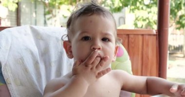 Kaşığıyla bebek maması yiyen bir çocuğun portresi. Anne, çocuğu dışarıda, çocukların masasında besliyor.