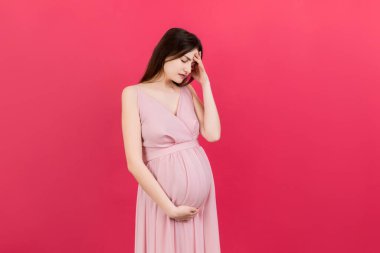 Güzel, genç, hamile bir kadın, renkli bir arka planda baş ağrısı çekiyor. Stresli hamile kadın ya da anne sorunları.