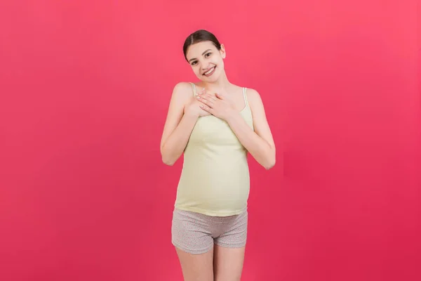年轻美丽的黑发女人怀孕了 怀着孩子 背对孤立的背景 双手放在胸前笑着 健康孕产概念 — 图库照片